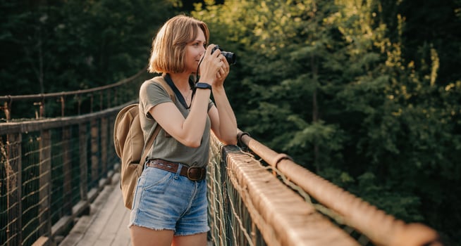 Attractive young female traveler photographing with camera while standing on the scenic bridge photo