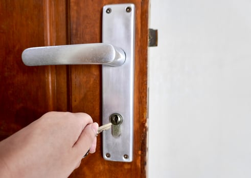 Hand holding key to unlock door knob isolated on horizontal brown door background. photo