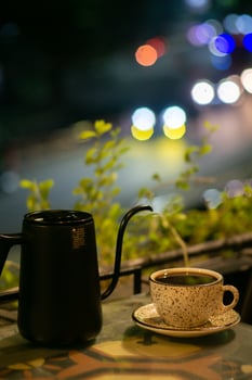 Cup of coffee and teapot on the table with blurred background photo