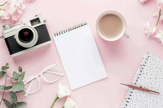 A cozy arrangement featuring a vintage camera, a blank journal, a steaming cup, and delicate flowers invites creativity and exploration. photo