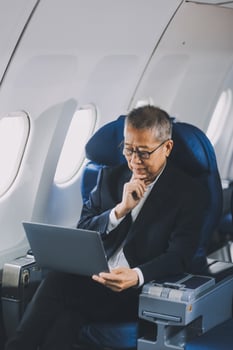 Attractive Asian male passenger of airplane sitting in comfortable seat while working laptop and tablet with mock up area using wireless connection. Travel in style, work with grace. photo