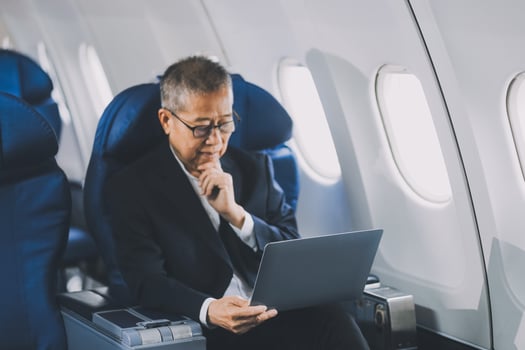 Attractive Asian male passenger of airplane sitting in comfortable seat while working laptop and tablet with mock up area using wireless connection. Travel in style, work with grace. photo