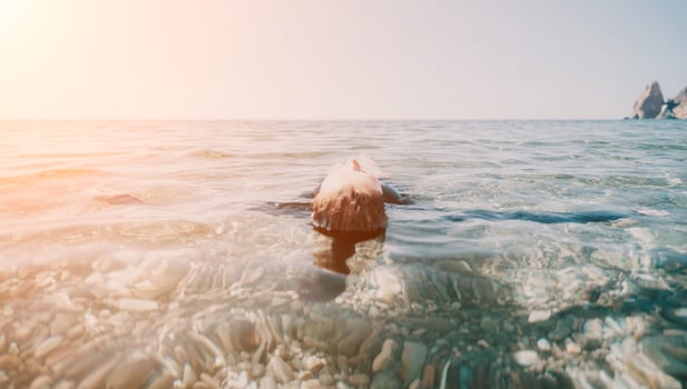 Woman swimming in sea at sunset, float on calm water back view. Concept of body image and fitness, enjoying a serene beach. Happy woman with perfect fit body enjoys sea beach photo