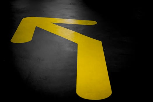 Yellow arrow on a dark asphalt surface, pointing towards the upper left corner, indicating directions photo