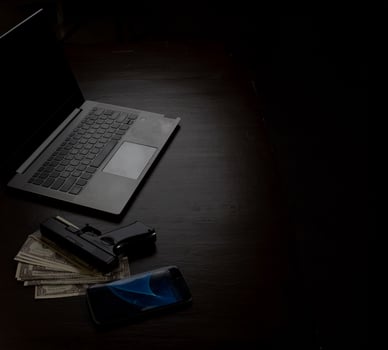 Computers, mobile phone, money, guns, and other devices that hackers use to steal or hijack information to trick victims into taking money. laying on wooden table in dark room in mysterious apartment. photo