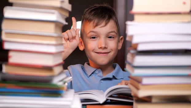 Smart young boy having an idea surrounded by a pile of books photo