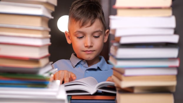 Young boy reading book surrounded by stacks of books photo