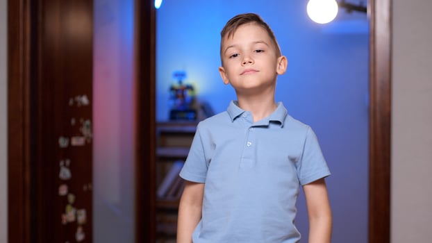 Confident young boy standing with hands on hips in room photo