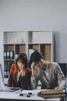 Stressed business couple working at big cabinet. Frustrated director closed face with hands at laptop workplace interior. Woman partner solving problems on smartphone call feeling nervous at office photo