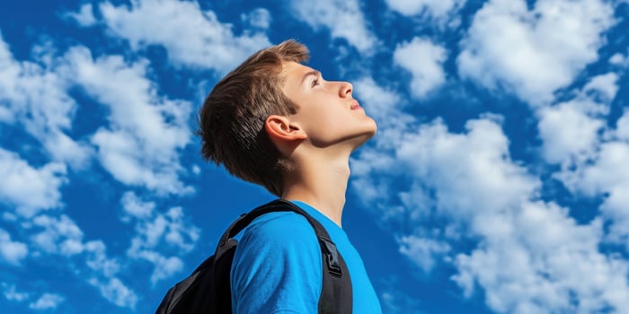 High school boy gazing up at a blue sky filled with clouds photo
