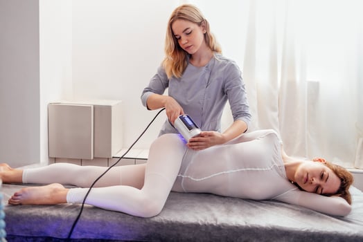 Beautician using massager to remove fat from hips of anonymous customer in salon photo