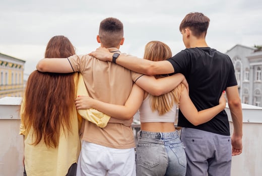 Four teenagers hug and stand with their backs on the roof of the house. Friends have a great time together. photo
