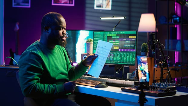 Artist pointing at musical sheet notation to explain notes on piano, teaching people to play synthesizer in home studio. Composer musician playing midi controller during online master class. Camera A. photo