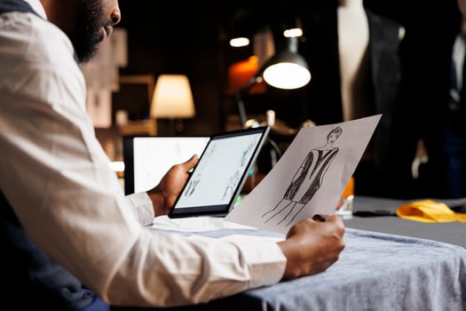 Dressmaker meticulously analyzing online sketch designs of fashion outfits displayed on tablet in tailoring studio. Tailor looking for inspiration for upcoming sartorial custom handmade collection photo