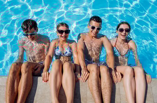 Cute teens friends in swimsuits and sunglasses are laughing in the pool. Smiling boys and girls having fun in the clear water. photo