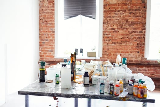 Modern interior of the art workshop or studio. Buckets with paint, dirty glass jars, brushes, spray gun, solvents and other art supplies are on the artist table. photo