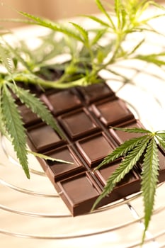 Dark chocolate bar placed beside fresh cannabis leaves on a marble background photo