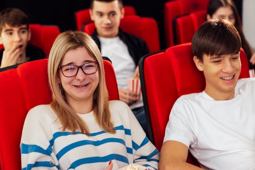 Nice young people in the cinema hall. A cute girl with glasses and popcorn and a guy are sitting in chairs and laughing while waiting for a movie. photo