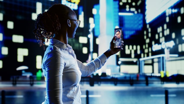 African american woman in videocall with boyfriend while strolling around city streets at night. Person using smartphone to show friend urban surroundings in dimly illuminated town centre photo