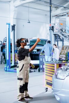 Certified mechanic in repair shop using VR googles and augmented reality hologram to visualize car parts in order to fix them. BIPOC woman using AR technology while working on broken vehicle brakes photo