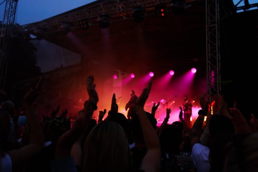 Silhouettes of crowd at concert in front of stage with bright spotlights. People enjoy live music at the band's performance. Concert hall with musicians on stage and fans during music festival photo