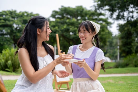 Two pretty and positive young Asian women are enjoying a picnic together in a green park. photo