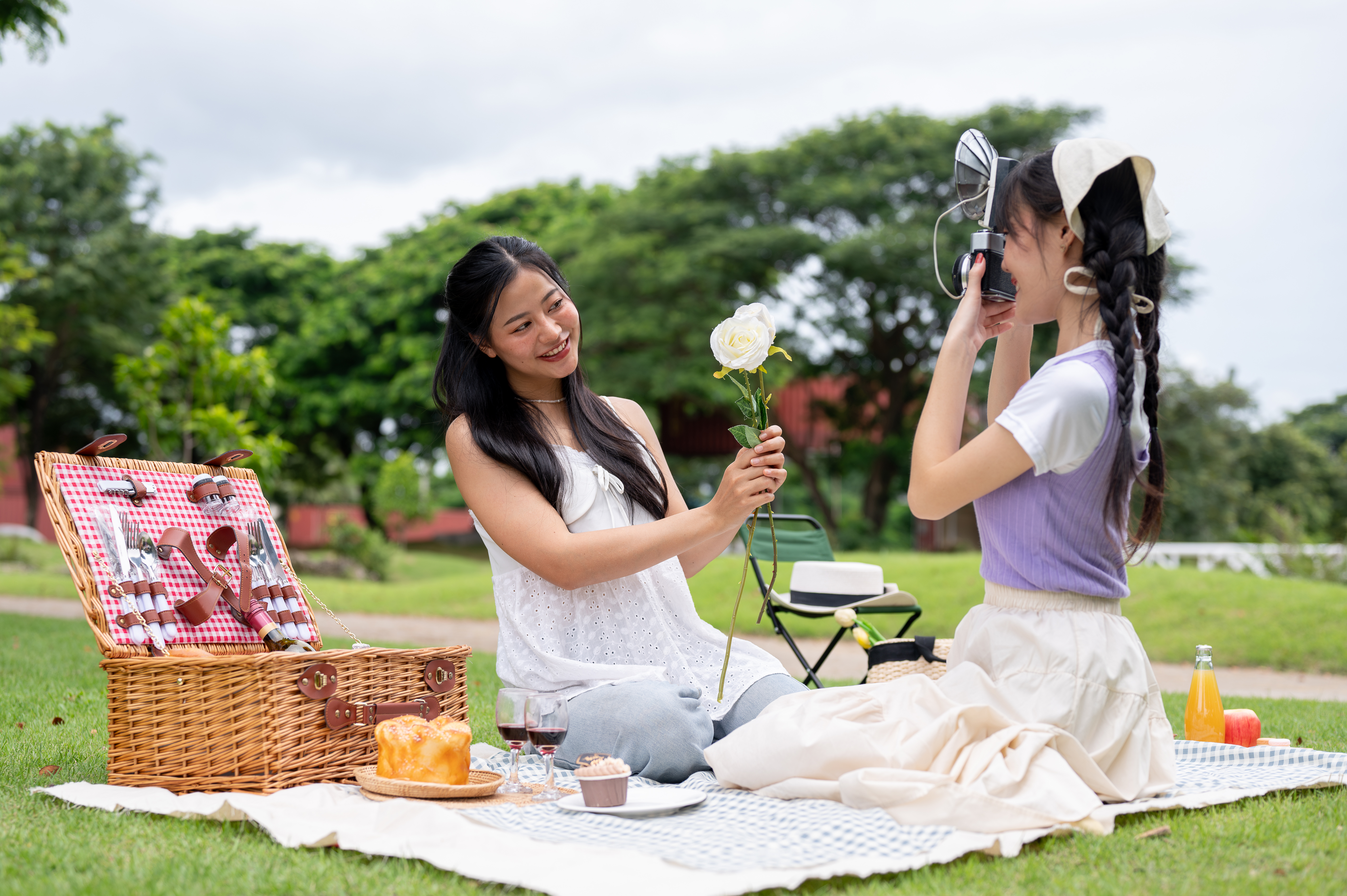 A happy Asian woman takes a picture of her friend with a retro camera while they enjoy a picnic. photo