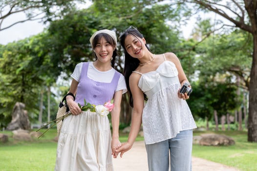 Two lovely Asian women are holding hands, strolling through a park, and smiling at the camera. photo