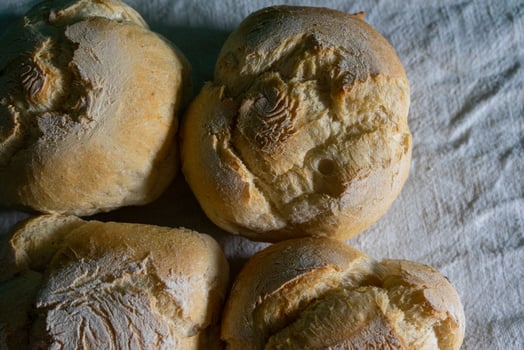 A closeup shot of traditional Alentejan bread rolls, known as papo-secos, freshly baked with a golden crust, displayed on a rustic wooden surface, showcasing their texture and artisanal quality. photo