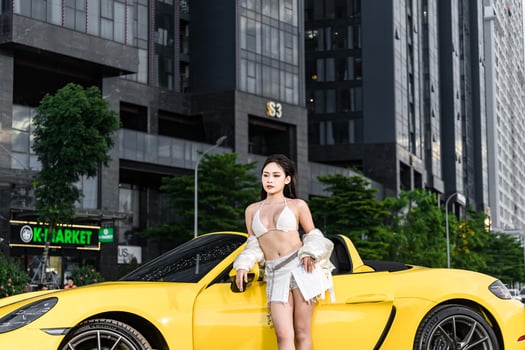 Hanoi, Vietnam - 26 Jun 2024 Beautiful young woman wearing bikini with Porsche 718 Boxster parked on the street during fashion photoshoot. photo