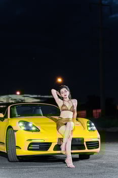 Hanoi, Vietnam - 26 Jun 2024 Beautiful young woman wearing bikini with Porsche 718 Boxster parked on the street during fashion photoshoot. photo