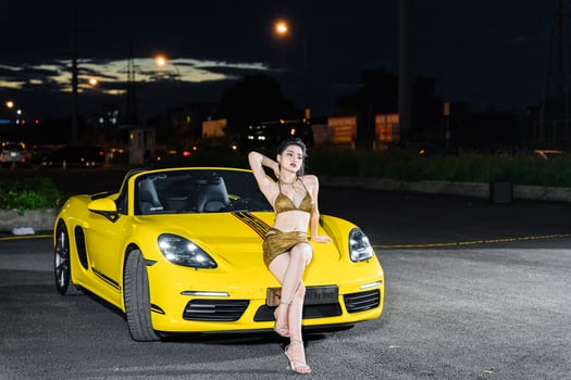 Hanoi, Vietnam - 26 Jun 2024 Beautiful young woman wearing bikini with Porsche 718 Boxster parked on the street during fashion photoshoot. photo