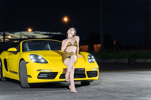Hanoi, Vietnam - 26 Jun 2024 Beautiful young woman wearing bikini with Porsche 718 Boxster parked on the street during fashion photoshoot. photo