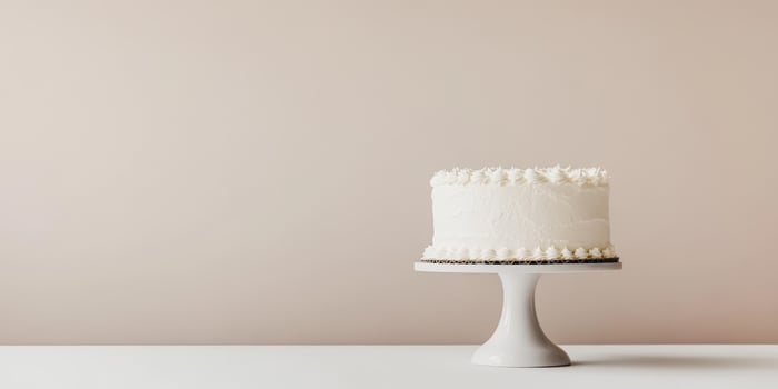 This is a beautifully minimalistic white birthday cake that is elegantly displayed on a lovely and simple cake stand, which is set against a soft and charming background that enhances its appearance photo