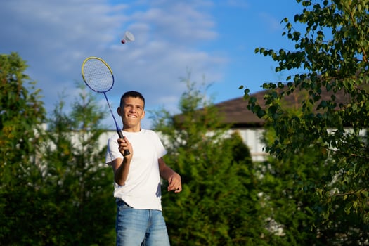Boy playing badminton outdoors in a sunny backyard with trees photo
