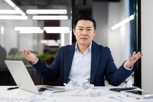 Serious office administrator raising arms aside while sitting by overloaded table with crumpled papers and pc. Busy male struggling with amount of work while coming back to office after vacation. photo