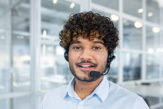 A young professional man smiles while wearing a headset in a brightly lit modern office environment, portraying customer support and professional assistance. photo