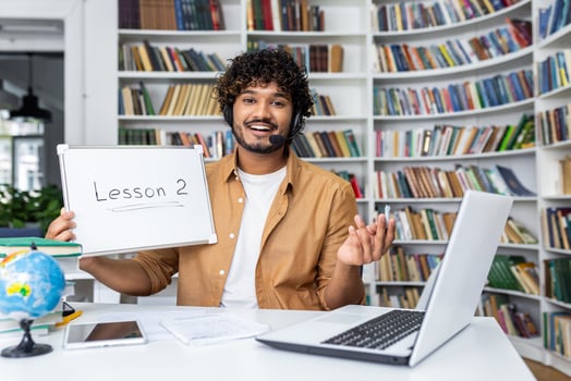 An enthusiastic online teacher giving a lesson from a home office with a whiteboard and a laptop in a bookshelf background. photo