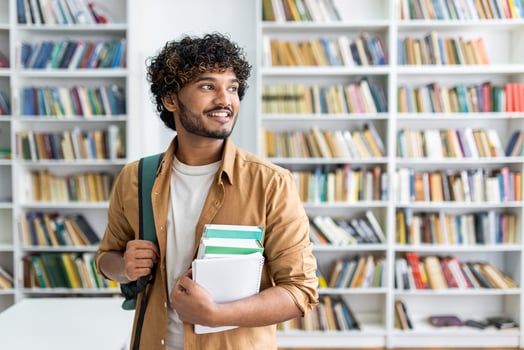 Young male student with curly hair smiling and holding textbooks in a modern library setting, exuding confidence and preparedness. photo