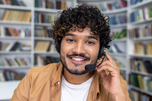 Focused student wearing a headset in a library adjusts his equipment, preparing for an online call with a teacher or peers. photo