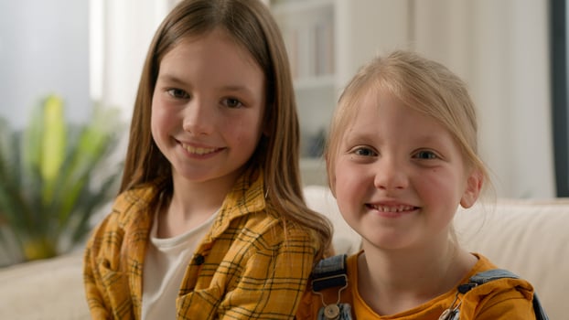 Two happy Caucasian children little girls daughters looking at camera together dental healthy toothy smile sisters kids friends posing relax showing positive emotion family couch living room indoors photo
