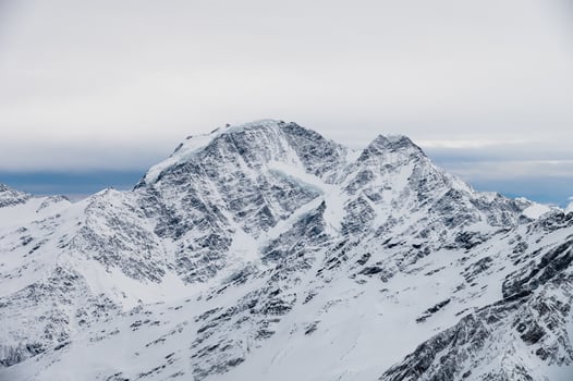 Picturesque view of mountain range with snow capped rocks under blue sky with white big cloud hanging over it in winter season photo