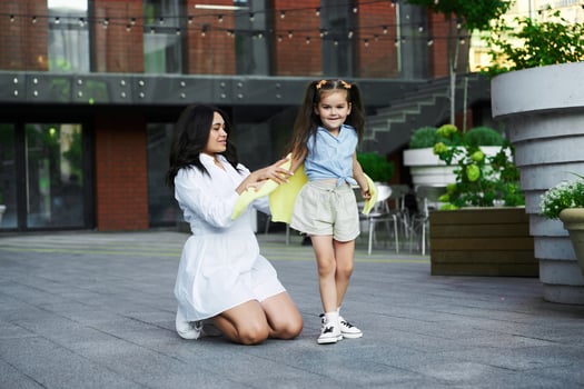 Mother helping her daughter put on a yellow cape in an urban park during sunset photo