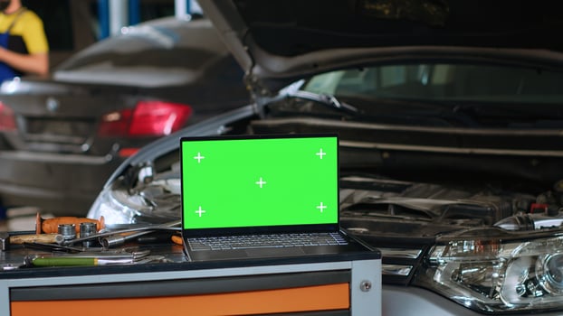 Close up panning shot of green screen laptop in auto repair shop, sitting on work bench next to professional mechanic tools in front of car with hood up waiting to be repaired photo