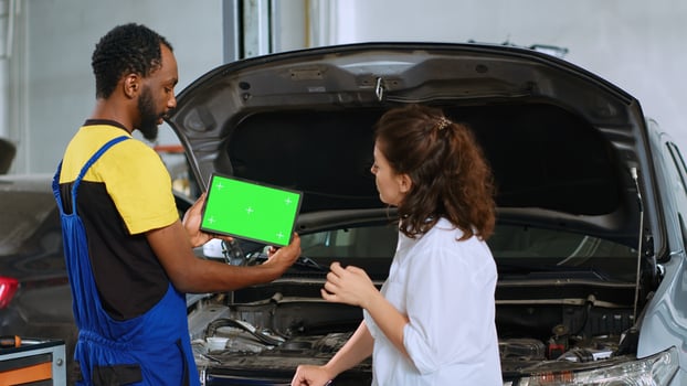 African american mechanic using green screen laptop to show woman damaged components found in her car. Repairman using mockup device to help client visualize repairments to be done to vehicle photo