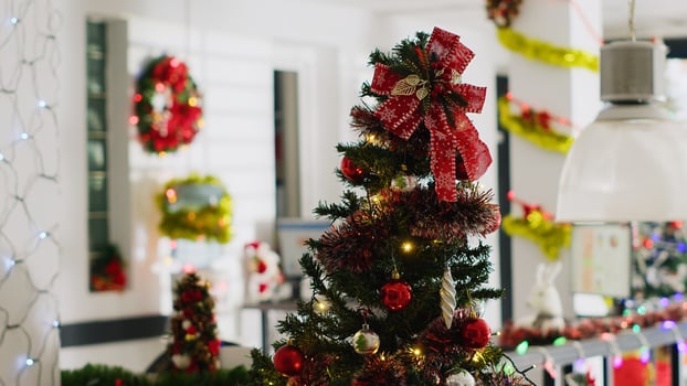 Christmas pine tree adorn with red ornaments in empty office, with blurry background of computer monitors on desks in xmas decorated workplace during winter holiday season photo