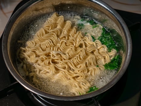 instant noodles and a few vegetables being cooked on the stove with boiling water photo