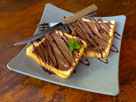 Slice of bread with chocolate swirl cream on blue plate. wooden background photo