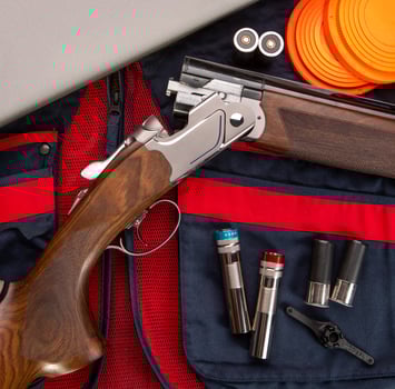 Double-barreled vertical shotgun and cartridges for it on a sports shooting vest. Shooting sport poster concept. Clay target plates for shooting with rifle on wooden back photo