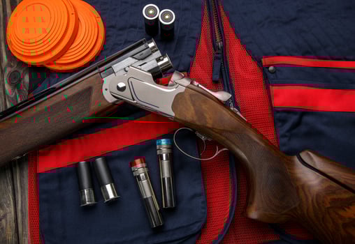 Double-barreled vertical shotgun and cartridges for it on a sports shooting vest. Shooting sport poster concept. Clay target plates for shooting with rifle on wooden back photo